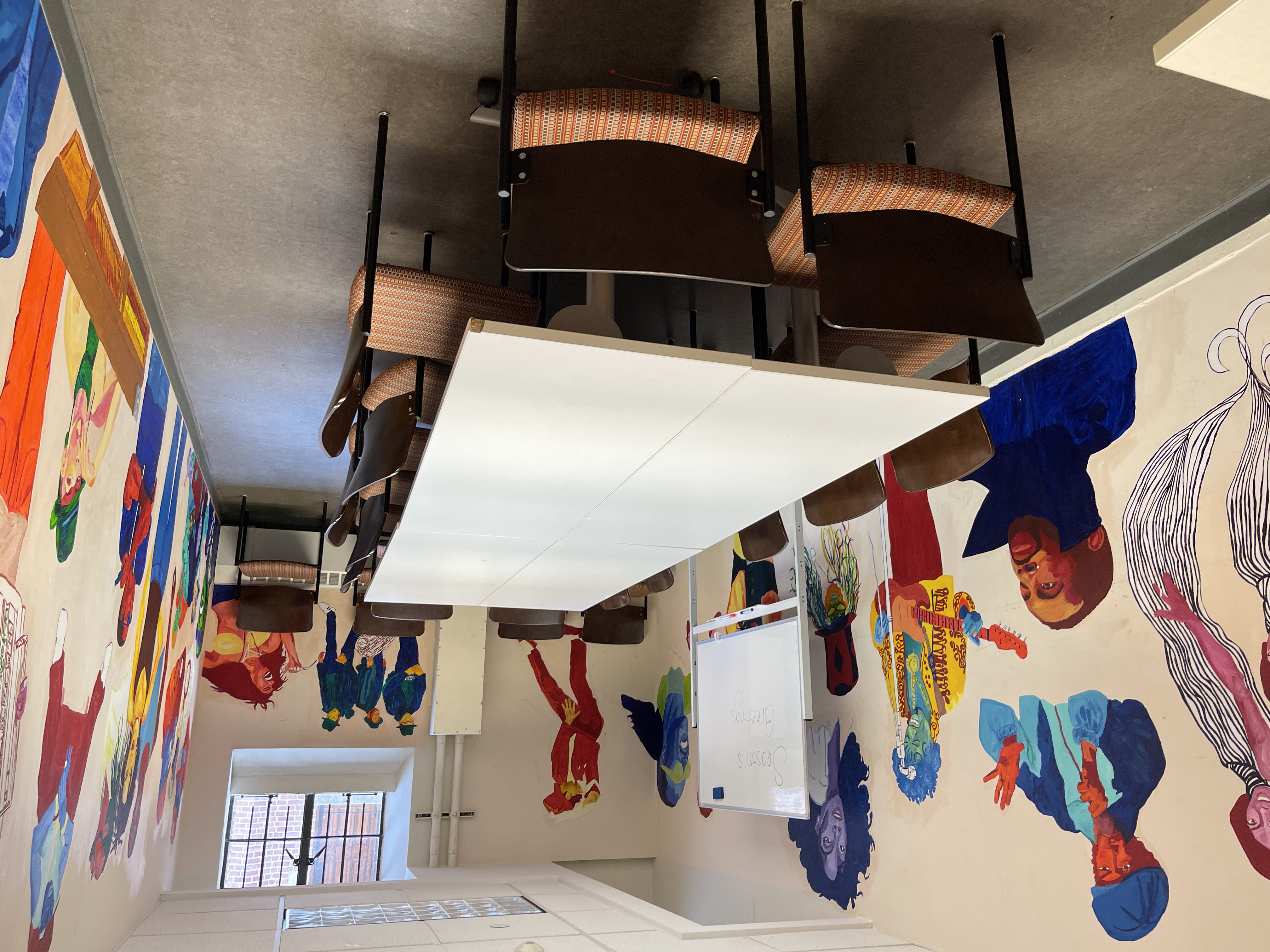 small study space with 16 seats around a long table and paintings of Black musicians along the walls; includes a whiteboard for group study sessions